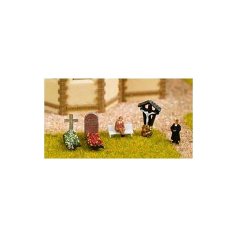 Miniatura cmentarza, postacie duchownego i osoby siedzącej, krzyż, nagrobki i ławka.